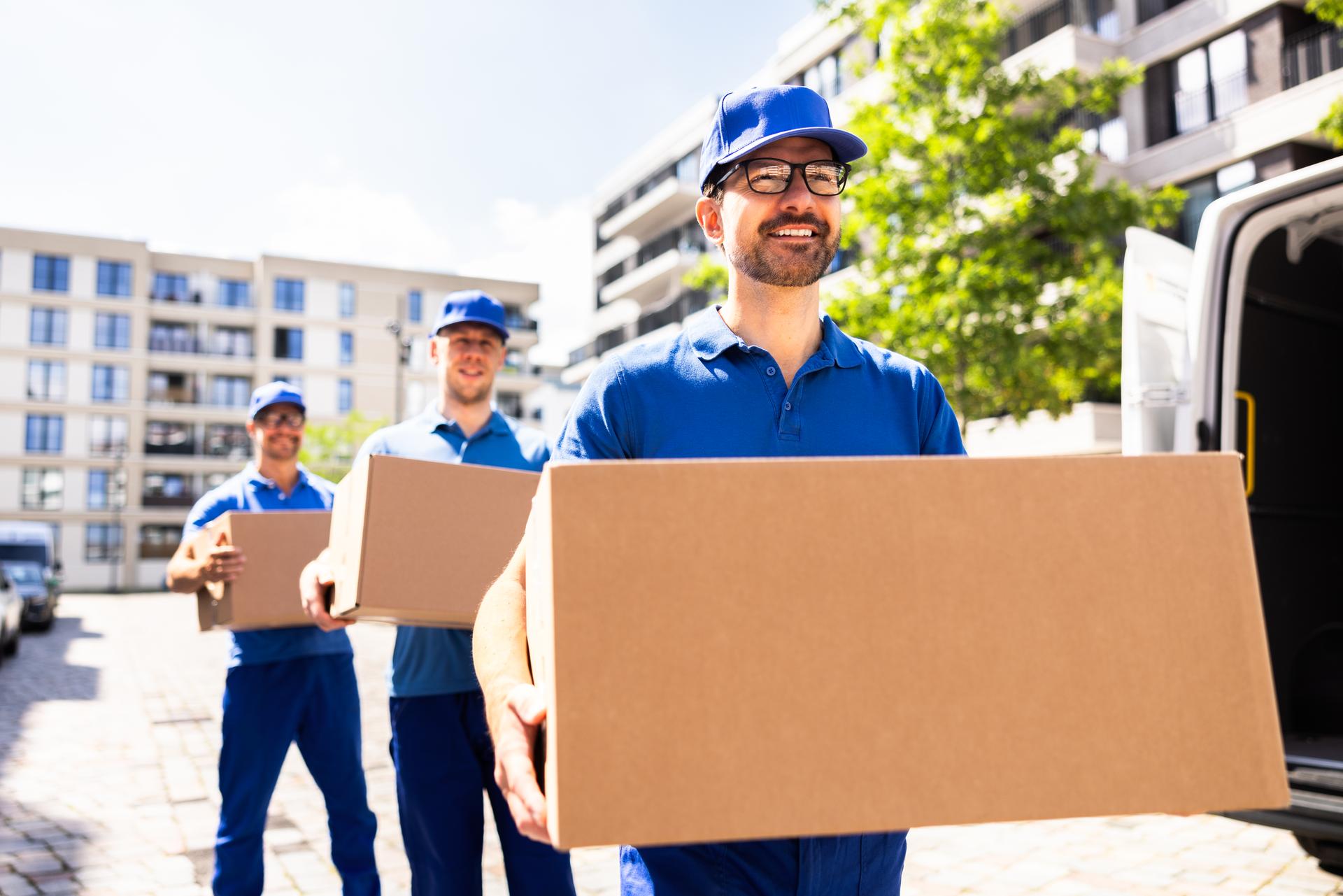 Delivery Man Pushes Hand Truck Trolley Full of Cardboard Boxes Hands Package to a Customer. Courier Delivers Parcel to Man in Business District.