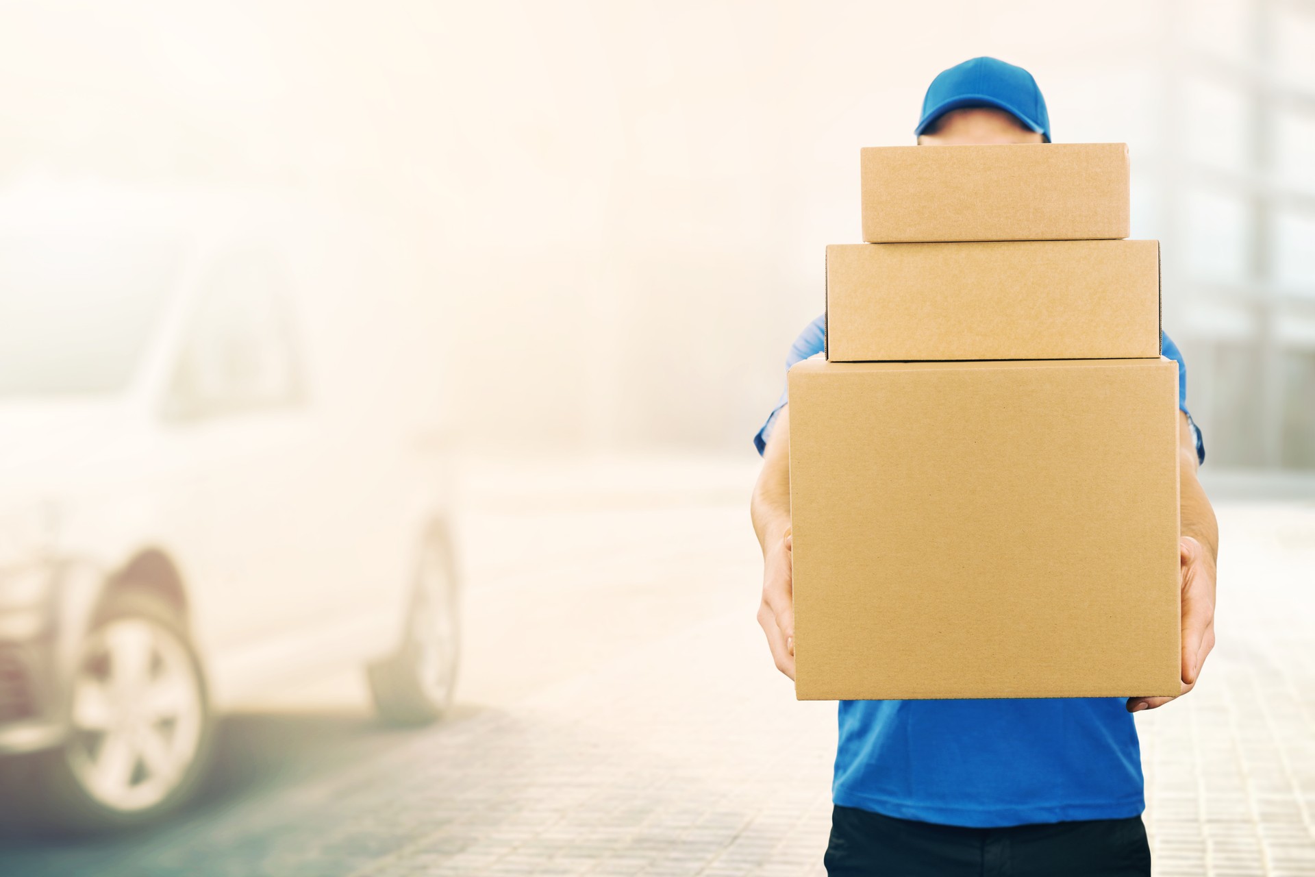 delivery man holding pile of cardboard boxes in front